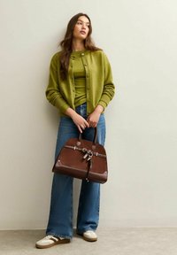 Bruine handtas met sleutelaccenten, gecombineerd met een groene cardigan en top, high-waisted blauwe jeans en beige sneakers met bruine strepen.
