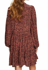 Robe en tissu marron avec un imprimé léopard noir et rose, dotée de manches longues et d'un ourlet volanté avec un design en niveaux.