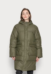 Piumino verde con cappuccio, realizzato in un materiale lucido. Presenta una chiusura con zip frontale, due tasche anteriori e un design di lunghezza media fino alla coscia.