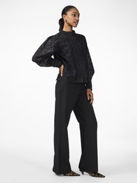 Black embroidered jacket with puffed sleeves, button front, and floral cutouts paired with black wide-leg trousers and leopard-print heels.