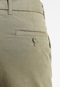Pantalon en coton kaki avec une texture lisse, doté d'une poche latérale, d'une fermeture par bouton de la même teinte et de détails de couture subtils.
