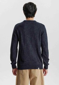 Granatowy sweter dzianinowy o teksturowym wykończeniu, z prążkowanymi mankietami i dołem oraz okrągłym dekoltem. Wykończony małą metką z logo na dole.