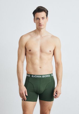 Grønne boksershorts med en kontrasterende svart midjebånd som har "BJÖRN BORG" i hvit tekst. Glatt stoff med en tettsittende design.