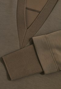 Brauner Sweatshirtstoff mit einem gerippten Bündchen und V-förmigem Design. Texturierte Bereiche weisen unterschiedliche Brauntöne und glatte Oberflächen auf.