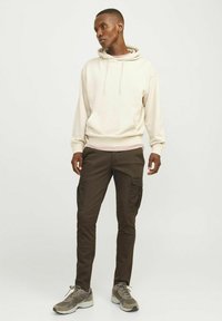Beige hoodie met een voorzak en trekkoorddetails, gecombineerd met donkerbruine cargo broek met zijzakken. Grijze sportschoenen.