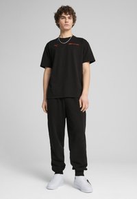 Czarny bawełniany T-shirt z krótkimi rękawami z czerwonym logo "Formula 1", w połączeniu z czarnymi dresami i białymi trampkami.