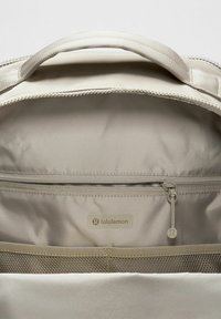 Béžová taška Lululemon s vnútorným pohľadom na zips zahŕňajúci pútko so značkou a sieťové organizačné vrecká nižšie.