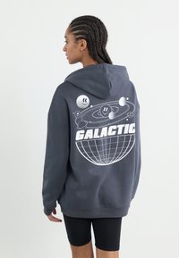 Felpa grigia con cappuccio e una grande grafica bianca di un globo e corpi celesti sul retro. Il testo recita "GALATTICO" in carattere grassetto.