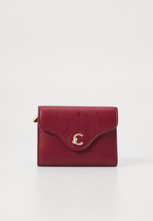 Burgundy leather wallet with a textured finish, curved flap, and a gold-tone initial accent on the front. Compact and rectangular shape.