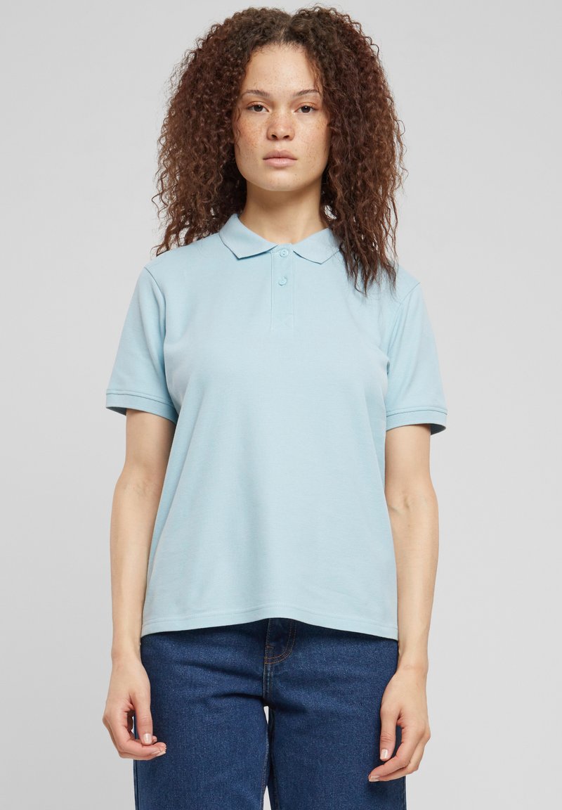 Šviesiai mėlyna polo marškinėliai su klasikiniu apykakliu, dviem mygtukais ir trumpomis rankovėmis, derinami su tamsiai mėlynais džinsais. Minkšta audinio tekstūra.