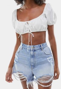 Vit kortärmad topp med puffärmar och dragsko, kombinerad med ljusblå slitna denimshorts med fransar i fållen och fickor.