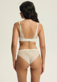 Biały komplet bielizny koronkowej składający się z biustonosza z regulowanymi ramiączkami i zapięciem na haftkę, w zestawie z majtkami wykończonymi koronką, zdobionymi kwiatowym wzorem.