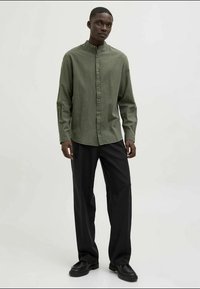 Camicetta verde oliva con colletto rialzato, abbinata a pantaloni neri, caratterizzati da una vestibilità comoda e una texture del tessuto liscia.