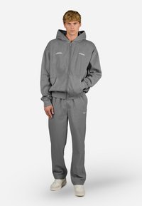 Grå lynlåshoodie med frontlommer, ledsaget af matchende grå sweatpants. Har logo detaljer og en afslappet pasform. Skoene er off-white.