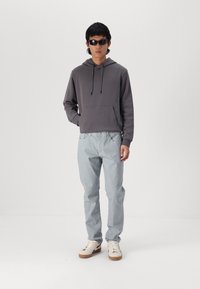 Grå hettegenser med frontlomme, lyseblå denimjeans og kremfargede sneakers. Sorte solbriller fullfører antrekket.