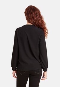 Haut noir à manches longues, texture côtelée, encolure ronde et coupe décontractée. Associé à un pantalon noir avec des coutures contrastantes sur les poches.