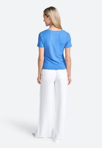 Maglietta azzurra a maniche corte con bordo ondulato abbinata a pantaloni bianchi a gamba larga, dotati di tasche posteriori e una texture liscia.
