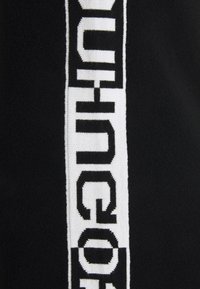 Tissu noir avec une bande blanche verticale ornée de grandes lettres noires en bloc formant un motif de texte abstrait.