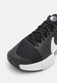 Black athletic shoe with a textured mesh upper, white logo accent, and rubber sole. Features laces and a streamlined, contoured design.