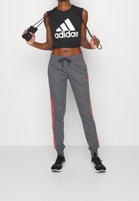 Musta lyhyt toppi, jossa valkoinen Adidas-logo, yhdistetty harmaisiin collegehousuihin, joissa on vaaleanpunaiset sivuraidat, sekä mustat urheilukengät.