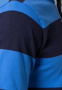 Gros plan d'un tissu rayé bleu et bleu marine sur un vêtement, montrant les détails de l'épaule et de la couture.