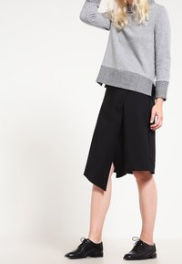 Szary sweter o teksturowanym wykończeniu, czarne culotki z asymetrycznym dołem oraz czarne sznurowane buty. Prosty, nowoczesny design.