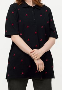 Polo noir à manches courtes et col, orné d'un motif répété de petites figures rouges. Tissu texturé, fermeture à boutons.