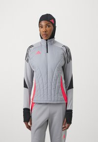 Chaqueta deportiva gris con cuello alto y cierre de cremallera. Acentos en negro y rosa, paneles texturizados y agujeros para el pulgar en las mangas.