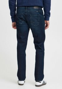 Mörkblå denimjeans med rak passform, med bakfickor och en etikett på midjan. Bärs med vita sneakers.