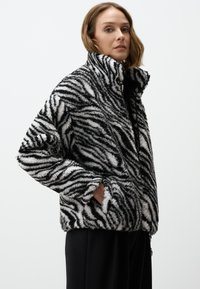 Zebra-gestreepte, pluche fleece jas met een hoge kraag en zijzakken; hoofdzakelijk zwart en wit met textuurstof.