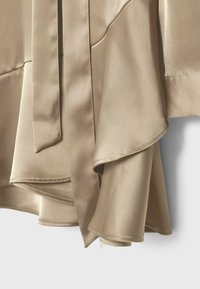 Tissu satin beige drapé avec des ourlets cousus et un détail de ceinture ou sangle suspendue, montrant une texture lisse et fluide.