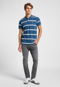 Polo blu con righe orizzontali bianche, maniche corte e colletto. Indossato con jeans grigi e sneakers bianche con righe nere.
