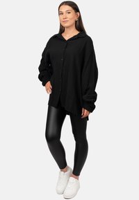 Camicetta nera con bottoni, in tessuto testurizzato e vestibilità comoda, abbinata a leggings neri lucidi e sneakers bianche.