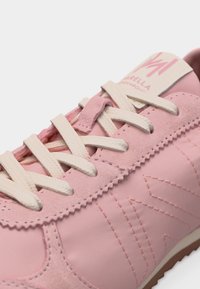 Ροζ αθλητικό παπούτσι με λευκά κορδόνια, υφές από σουέτ και δέρμα, και κεντητό μοτίβο "W" κατά μήκος της πλευράς.