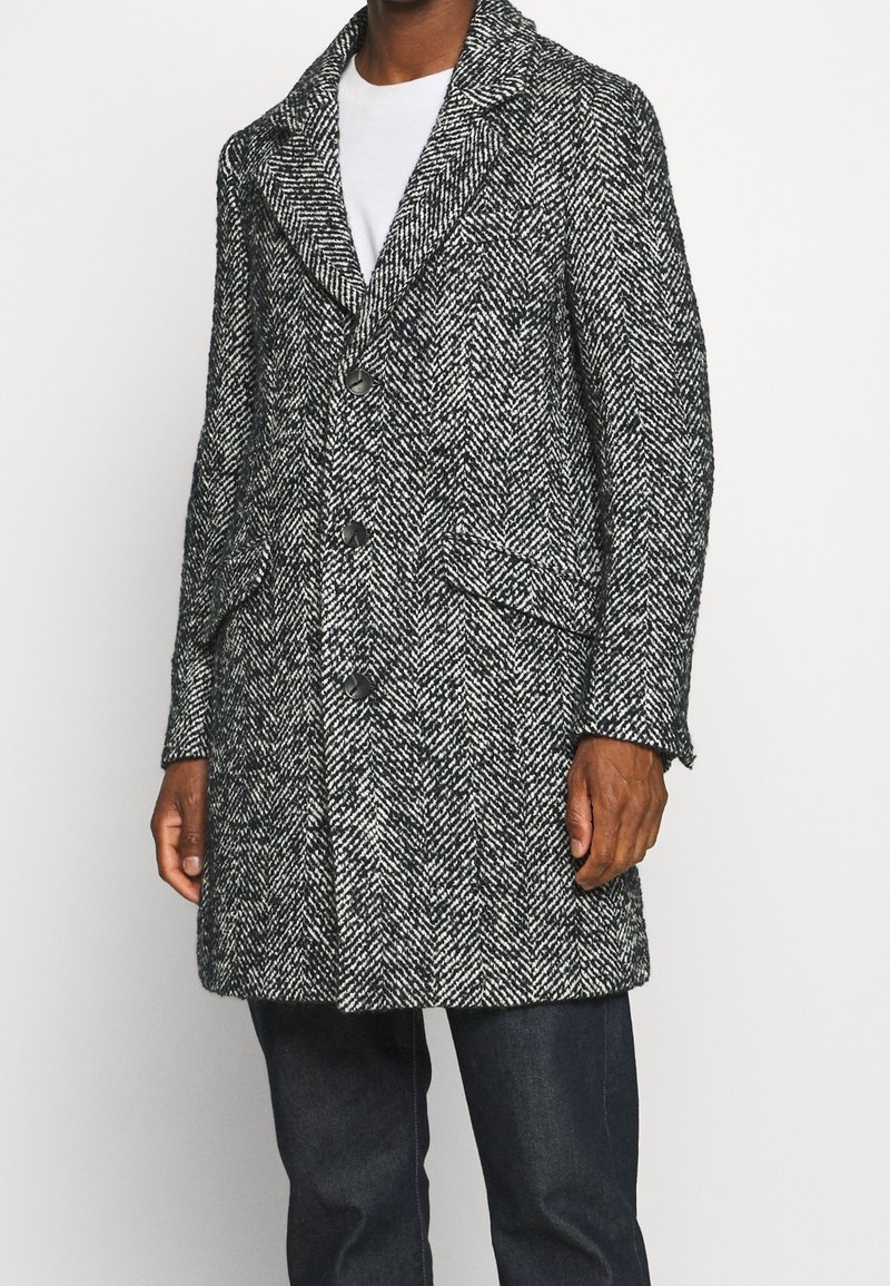 Cappotto grigio con motivo a spina di pesce, caratterizzato da un colletto a revers, chiusura con bottoni e due tasche frontali. Realizzato in tessuto strutturato.