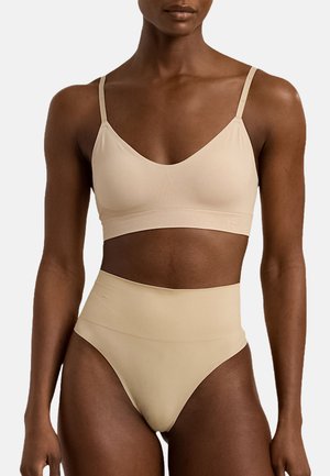 Beige wireless bralette with adjustable straps, featuring smooth texture and minimal seams, paired with high-waisted, seamless beige underwear.