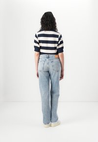 Gestreepte marineblauwe en witte top met korte mouwen, gecombineerd met lichtblauwe rechte jeans, voorzien van een achterzak en merklabel.
