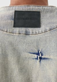 Hele sinine teksashirt musta nahkplaadi jaotusega krael. Seljal on erilised sinised õmblused.