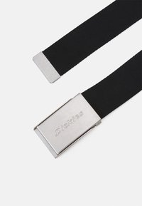 Sort elastisk bælte med en sølvmetalknap, der har det indgraverede brandnavn. Knapperne har kvadratiske kanter og en glat overflade.