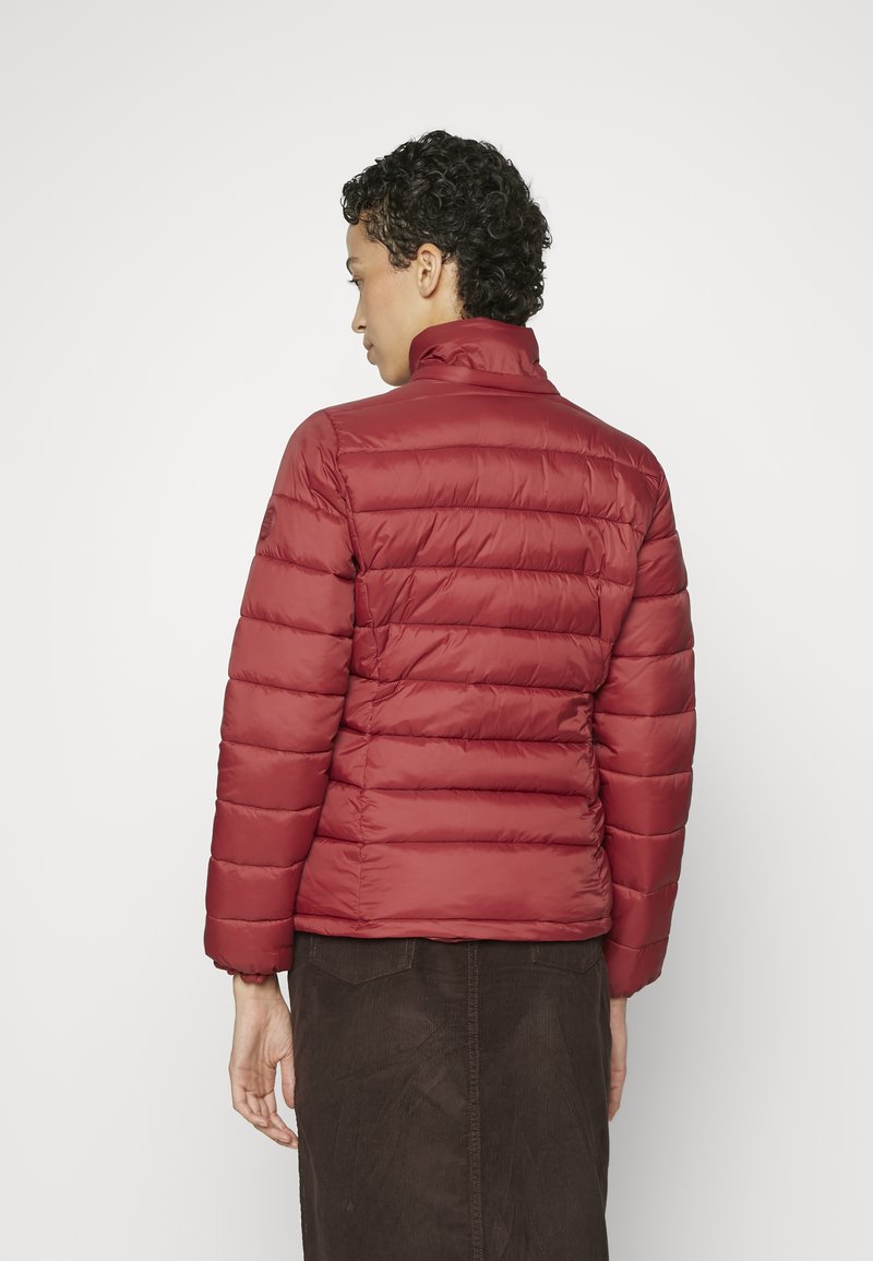 Chaqueta de plumas aislante roja con un cuello alto, que presenta un acolchado horizontal y un acabado suave. Llevada sobre una falda marrón texturizada.
