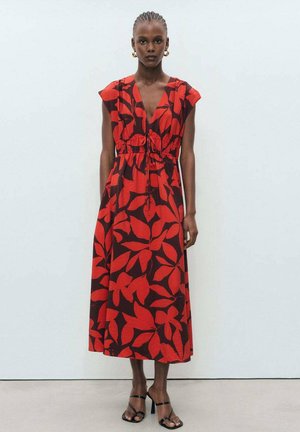Rotes und braunes Blumenkleid im Maxi-Stil mit kurzen Ärmeln, elastischem Bund und tiefem V-Ausschnitt. Getragen mit schwarzen Riemchensandalen.