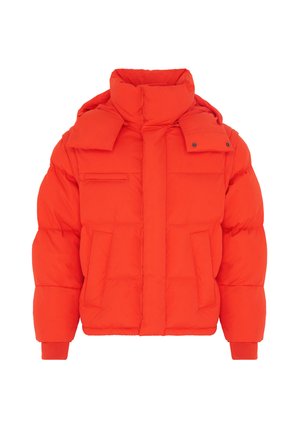 Personne portant une doudoune orange vif, un bonnet noir, un t-shirt noir à manches longues et un pantalon cargo noir ample, debout devant un fond gris.