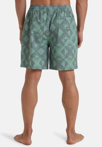 Costume de baie cu model verde, având un design geometric cu forme abstracte. Include un brâu elastic și un buzunar la spate.