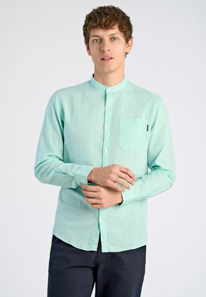 Camisa de manga larga verde menta claro con cuello mao, bolsillo frontal y cierres de botón. La tela tiene una textura sutil y un brillo.
