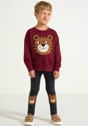 Maroon sweatshirt med tigermotiv, tillsammans med marinblå leggings som har tigermärken på knäna. Beige skor fulländar outfiten.