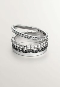 Anillos apilados de plata con texturas variadas; incluyen piedras claras y negras, acentos en pirámide, y acabados lisos.
