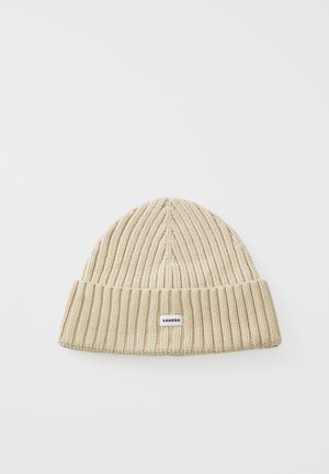 Knit beanie in light beige, featuring a ribbed texture and a folded cuff; small brand tag attached at the front.
