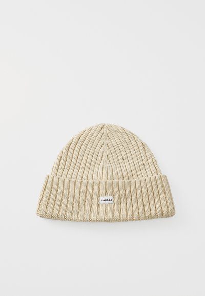 Bonnet en tricot de couleur beige clair, avec une texture à côtes et un revers replié ; petite étiquette de la marque attachée à l'avant.