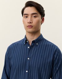 Tengerészkék gombos ing fehér függőleges csíkokkal, gallérral és egy kis hímezett logóval a bal oldalon. Puha anyag, sima textúrával.