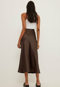 Brauner Satin-Midi-Rock mit glatter Textur, A-Linien-Form und Taillenbund. Kombiniert mit einem weißen Crop-Top und schwarzen Slippers.